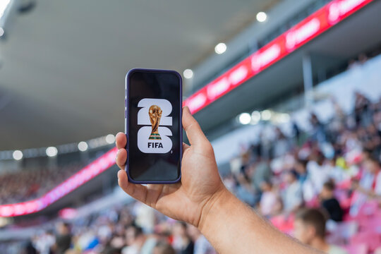 MINSK, BELARUS JUNE 9, 2026: Man holding a purple Apple iPhone 14 Pro in the stadium. The official logo of the football World Cup in the USA, Mexico, and Canada.