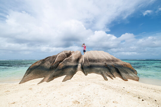 Tourist standing on top of granite rock in Seychelles and looking around at horizon. Solitude, freedom, outdoor exploration and travel destination concept.