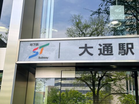 Odori Station subway entrance sign at the Semba Building with urban reflections of green trees and surrounding architecture in Sapporo city - Hokkaido, Japan, May 12, 2026