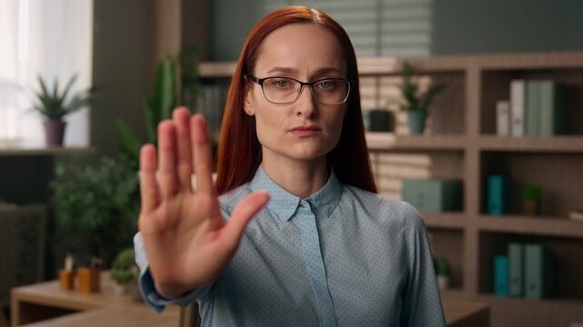 Serious Caucasian business woman showing stop gesture with hand looking at camera indoor office dissatisfied businesswoman leader girl confident female in glasses manager rejecting forbid warning sign