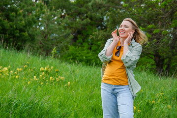 Fototapeta premium Serene happy woman standing with closed eyes in green meadow with yellow wild flowers. Enjoyment, sensory awareness, morning fresh air and wellness concept.