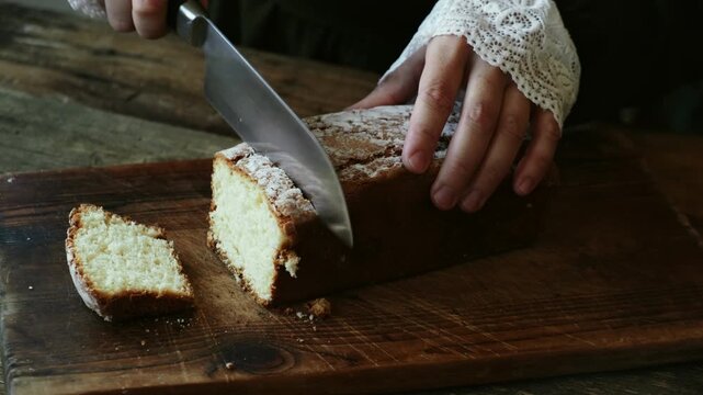 Close up hands slicing a baked biscuit cottage cheese cake with a knife. Fresh pastries sprinkled with powdered sugar, rustic style.