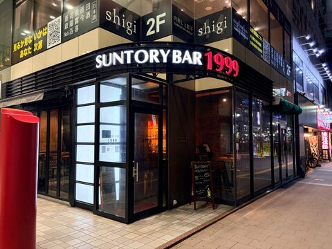 Suntory Bar 1999 and bar pavane entrance at night in the bustling Susukino entertainment district with illuminated signage and reflections - Hokkaido, Japan, May 9, 2026