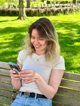 Happy young woman reading a message on smartphone sitting in a bench in a parking lot