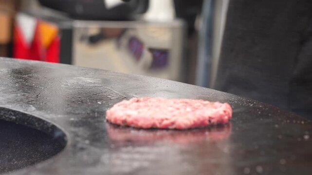 Outdoor cooking process of flattening fresh ground beef cutlet on a steaming hot plancha grill using professional kitchen tools and utensils