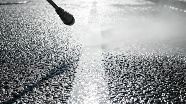 Pressure washer cleaning dirty asphalt driveway. High pressure steam nozzle removing grime from pavement. Residential exterior maintenance and home improvement task.