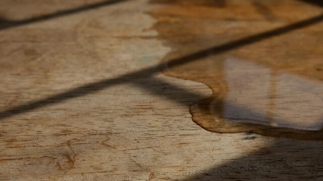 Macro close-up of thin water stream trickling across rustic aged wood grain surface with warm golden light and shadow in still life photography