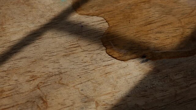 Macro close-up of thin water stream trickling across rustic aged wood grain surface with warm golden light and shadow in still life photography