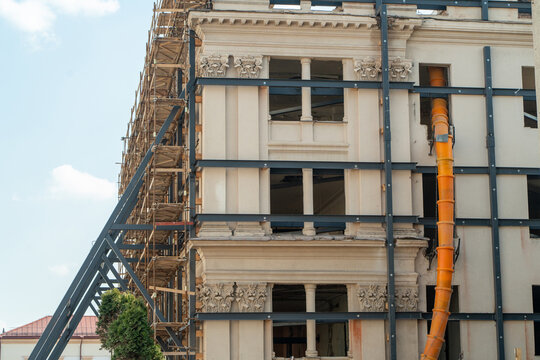 Repair and restoration of an old building. The steel beam structure supporting the reconstructed walls, Construction scaffolding and Suspended sections of a construction garbage chute on a building.