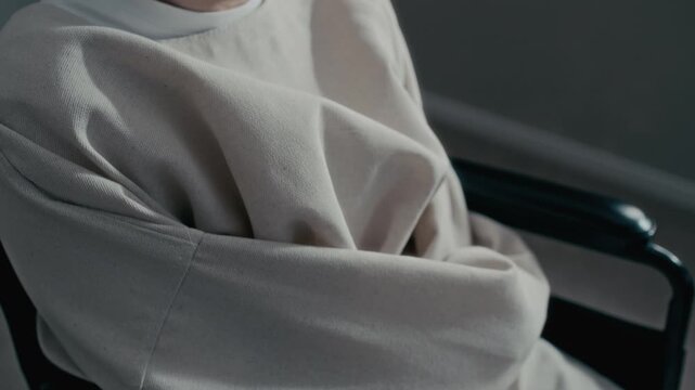Tilt up of middle aged Caucasian man with disability wearing straitjacket sitting in wheelchair, looking away. Footage ideal for psychiatric care and mental health awareness campaigns