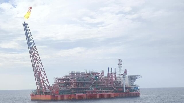 A large red and white floating production storage and offloading unit operates in the sea.