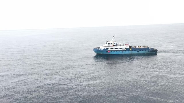 The industrial utility vessel navigates steadily through the deep ocean water, leaving a gentle wake behind.
