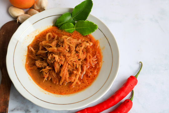 Spicy young papaya curry served in a rich coconut milk sauce, garnished with kaffir lime leaves and accompanied by fresh chili peppers. isolated on white marmer.