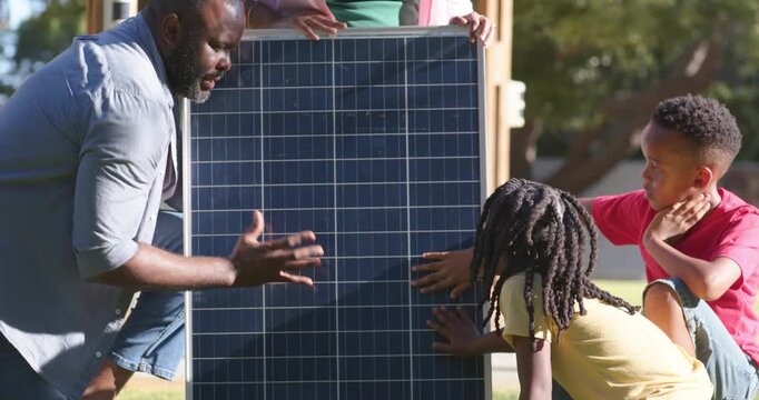 African American family learning as man guiding youth touching solar panel on lawn by wooden porch