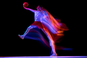 Obraz premium Basketball player leaping forward with neon trails on dark studio background. Concept of basketball performance, sport advertising, poster design, power, energy, scoring action.