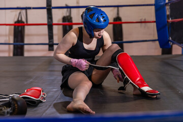 Red shin guard being fastened on padded boxing ring floor with blue headgear nearby © wavebreak3