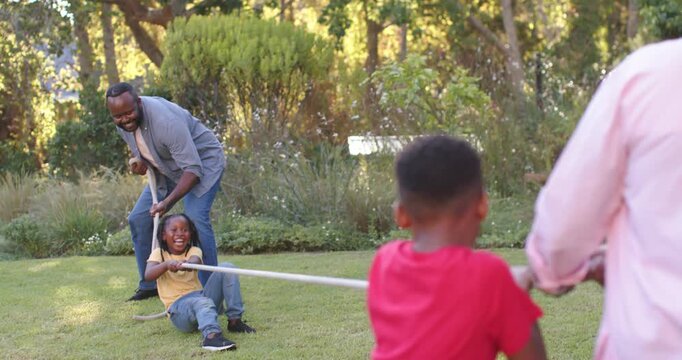African American family playing tug, rope taut on sunny lawn, girl yellow-top sliding, man bracing