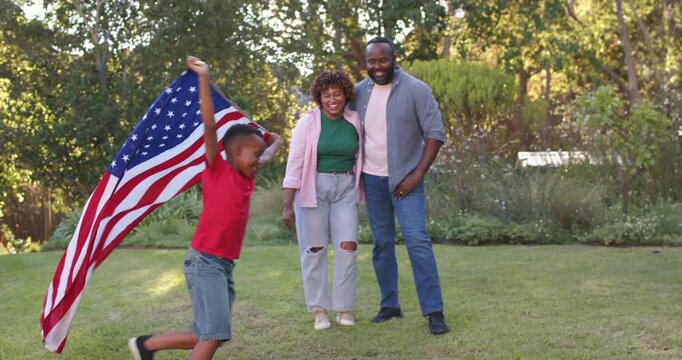 African American family on lawn watching son running from left waving large American flag playing