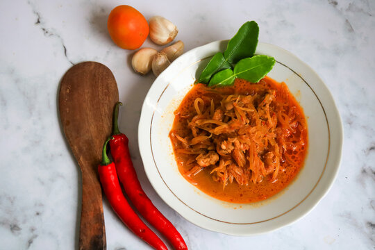 Spicy young papaya curry served in a rich coconut milk sauce, garnished with kaffir lime leaves and accompanied by fresh chili peppers. isolated on white marmer.
