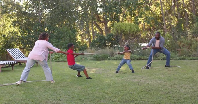 African American family with children grabbing rope, pulling and bracing on backyard lawn to play