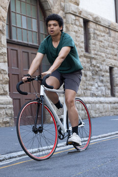 Adult African American male pedaling white fixed-gear bike with red rim by arched wooden door