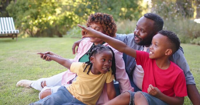 African American family spotting off-frame object, pointing up in park, with phone and small item