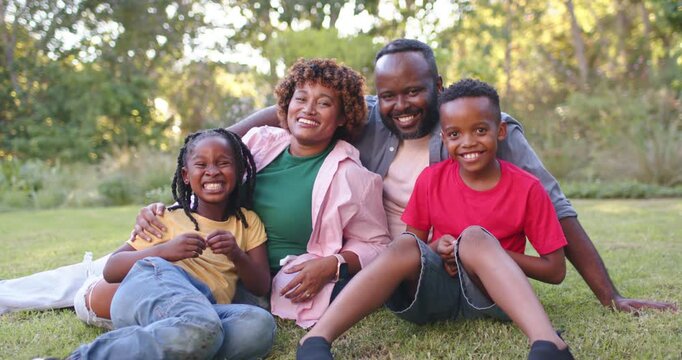 African American family posing, hugging on grass for portrait, camera prompt, smartwatch visible