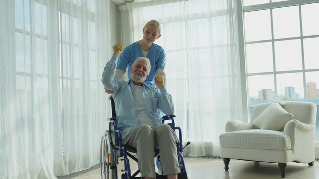 Support rehabilitation healthcare. Nurse helps old man patient in wheelchair picking up dumbbells. Paralyzed man in chair for people with disability doing sports exercise with nurse. Medical caregiver