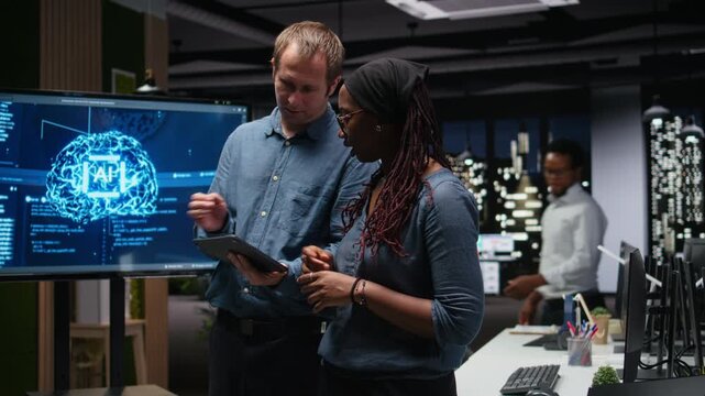 Engineering team in office analyzing machine learning using tablet and laptop. Coworkers discussing, using devices to improve AI prediction accuracy.