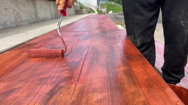 Man painting a wooden bench outside with the paint roller, furniture renovation video