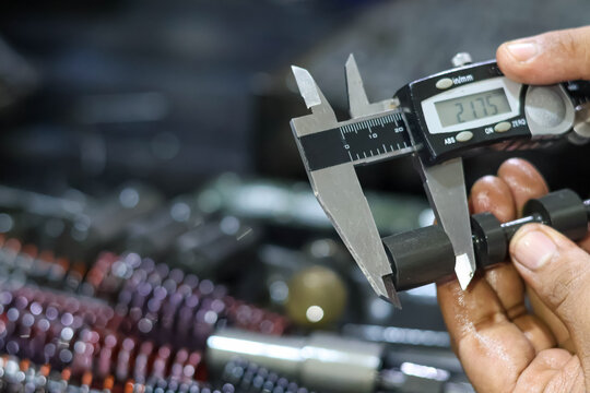 Close-up of mechanic hands using a digital vernier caliper to measure a metal engine part precisely in a workshop.