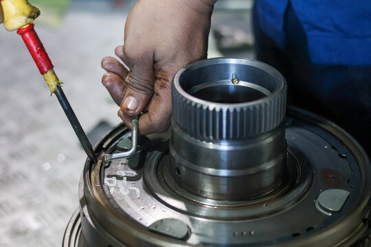 Close-up of mechanic hands using a screwdriver and a pick tool to install a metal retaining snap ring onto an automatic gearbox clutch drum assembly.