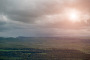 Fototapeta premium Bright sun breaking through heavy dark storm clouds over misty rolling hills. Hope concept, dramatic sunlight rays, weather contrast and changing atmosphere.