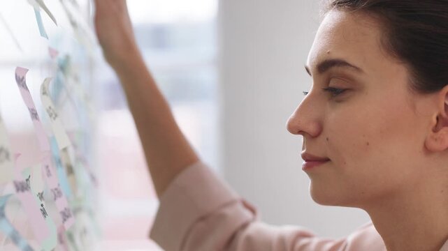 Woman, glass wall and sticky note at startup with project management, planning or review at office. Person, paper and job with solution, proposal or problem solving with schedule at creative agency