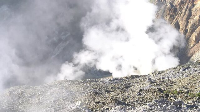 Volcanic landscape with steam rising from fumaroles in a rocky crater, showcasing geothermal activity and rugged terrain in a mountainous region