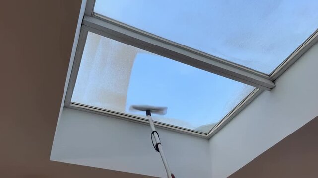 Cleaning skylight glass with extendable mop under clear blue sky