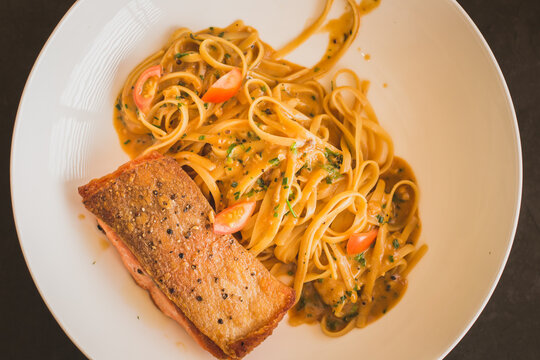 grilled salmon steak with linguine paste glazed in prawn bisque in a white ceramic dish