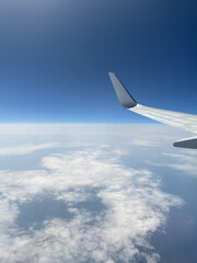 Obraz premium Aerial view of the earth from an aircraft wing above the clouds with a clear blue sky horizon. Flying airplane travel perspective, stratosphere flight altitude, high altitude passenger journey concept