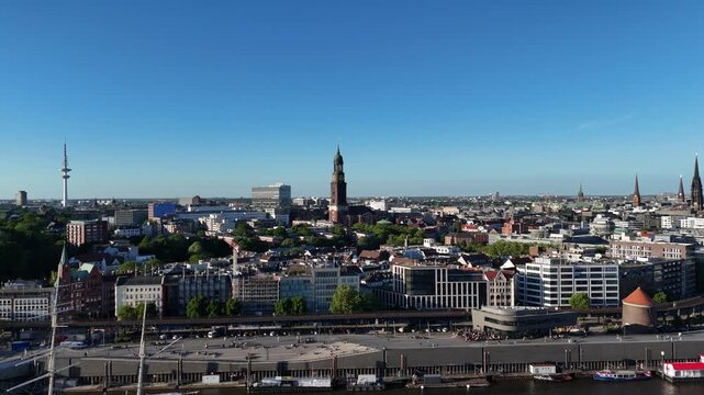 Rising drone move from left to right above Landungsbrucken, circling a church tower while the Hamburg Fernsehturm and city background appear.
