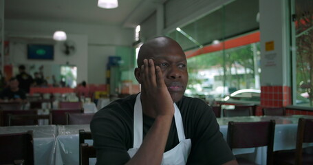 Obraz premium African American man in restaurant resting face in hand, looking off with thoughtful and slightly worried expression, close-up in indoor dining space