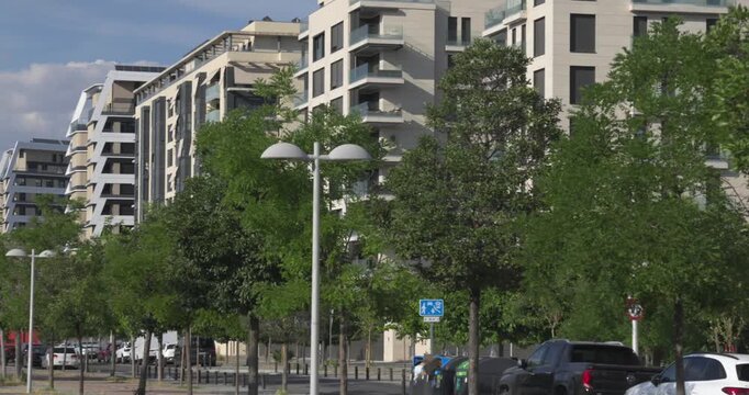 City street with lush trees, parked cars, and residential high-rise buildings
