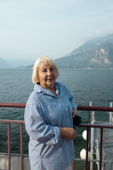 Fototapeta premium Portrait of a happy senior lady with grey hair showing beautiful landscape background on a sunny day during her retirement journey.