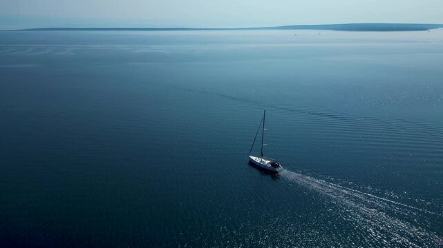 A stunning aerial drone perspective showcasing a white sailboat gliding through the crystal-clear, turquoise waters of Silba Island, Croatia. The shot beautifully captures the contrast between the