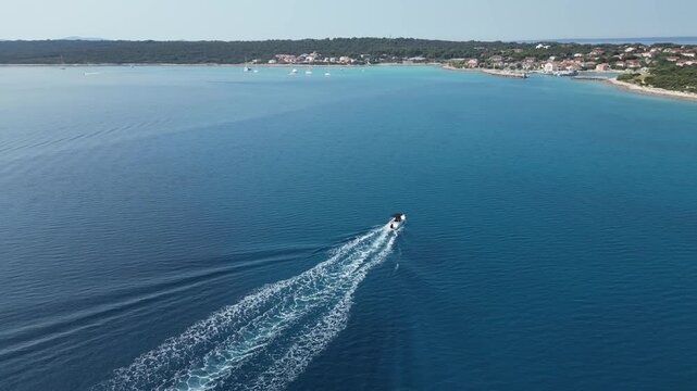 Aerial drone view of a speedboat approaching Silba Island in Croatia across the deep blue Adriatic Sea. Scenic Mediterranean coastline, turquoise waters and a charming island village create an idyllic