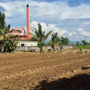 Traditional Thai temple crematorium chimney with plowed agricultural soil and palm trees background