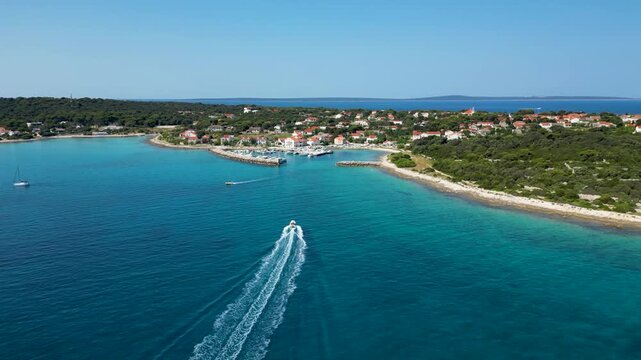 Aerial drone view of a speedboat approaching Silba Island in Croatia across the deep blue Adriatic Sea. Scenic Mediterranean coastline, turquoise waters and a charming island village create an idyllic