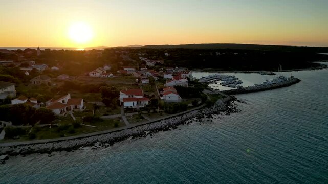 A stunning aerial drone shot capturing the warm golden sunset over the Sotorisce bay and Mulj harbor area on Silba Island, Croatia. The perspective showcases the sheltered marina filled with boats