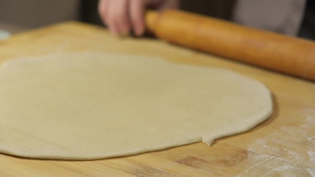 Rolling dough with hands and a wooden rolling pin on a kitchen table for baking