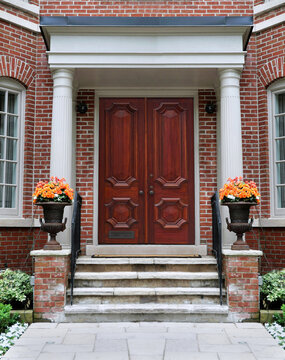 Elegant wood grain front door with columns and colorful flower pots