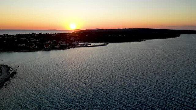 A stunning aerial drone shot capturing the warm golden sunset over the Sotorisce bay and Mulj harbor area on Silba Island, Croatia. The perspective showcases the sheltered marina filled with boats